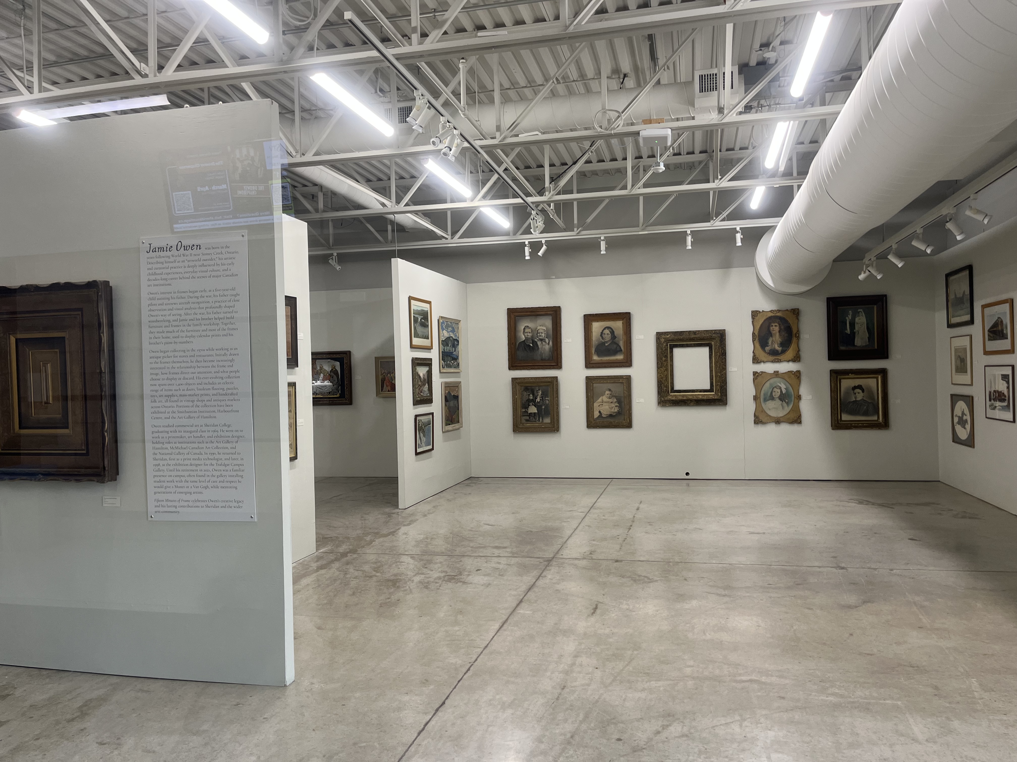 This photo captures the interior of Sheridan’s gallery space, featuring a curated collection of framed artworks displayed along clean white walls. The open floor plan and polished concrete flooring create a neutral environment that places full attention on the artwork. The exposed ceiling, lighting tracks, and large air duct emphasize an industrial aesthetic, contrasting with the historical and traditional style of many of the framed pieces. The space encourages slow movement and contemplation, as visitors can navigate around angled partition walls and view the art from multiple perspectives. Overall, this gallery showcases how spatial layout, lighting, and material choices work together to shape the experience of observing artwork.